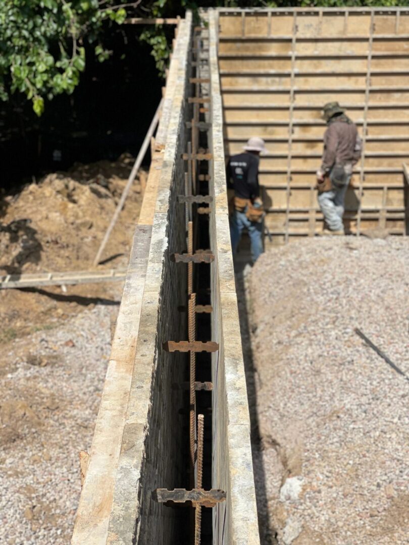 Construction workers building a concrete foundation wall at a site.