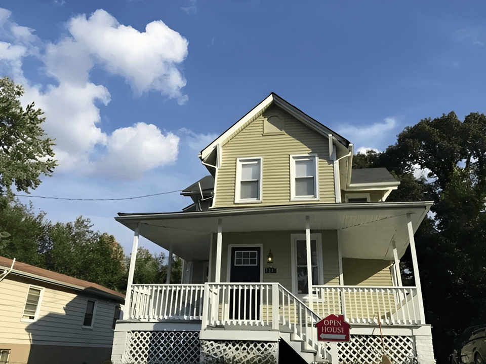 A two-story yellow house with a porch under a blue sky.